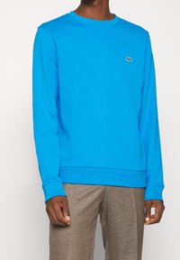 Sudadera azul de algodón, con cuello redondo, mangas largas y un sutil detalle de logo en el pecho. Detalle texturizado en la cintura.