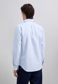 Camisa celeste con cuello, hecha de tela a rayas, con mangas largas, detalle de canesú en la parte trasera y puños con botones, combinada con vaqueros oscuros.