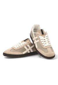 Zapatillas de ante y tela beige con rayas blancas, diseño de cordones, paneles texturizados y suelas de goma marrón. Rayas verticales destacadas en la lengüeta.