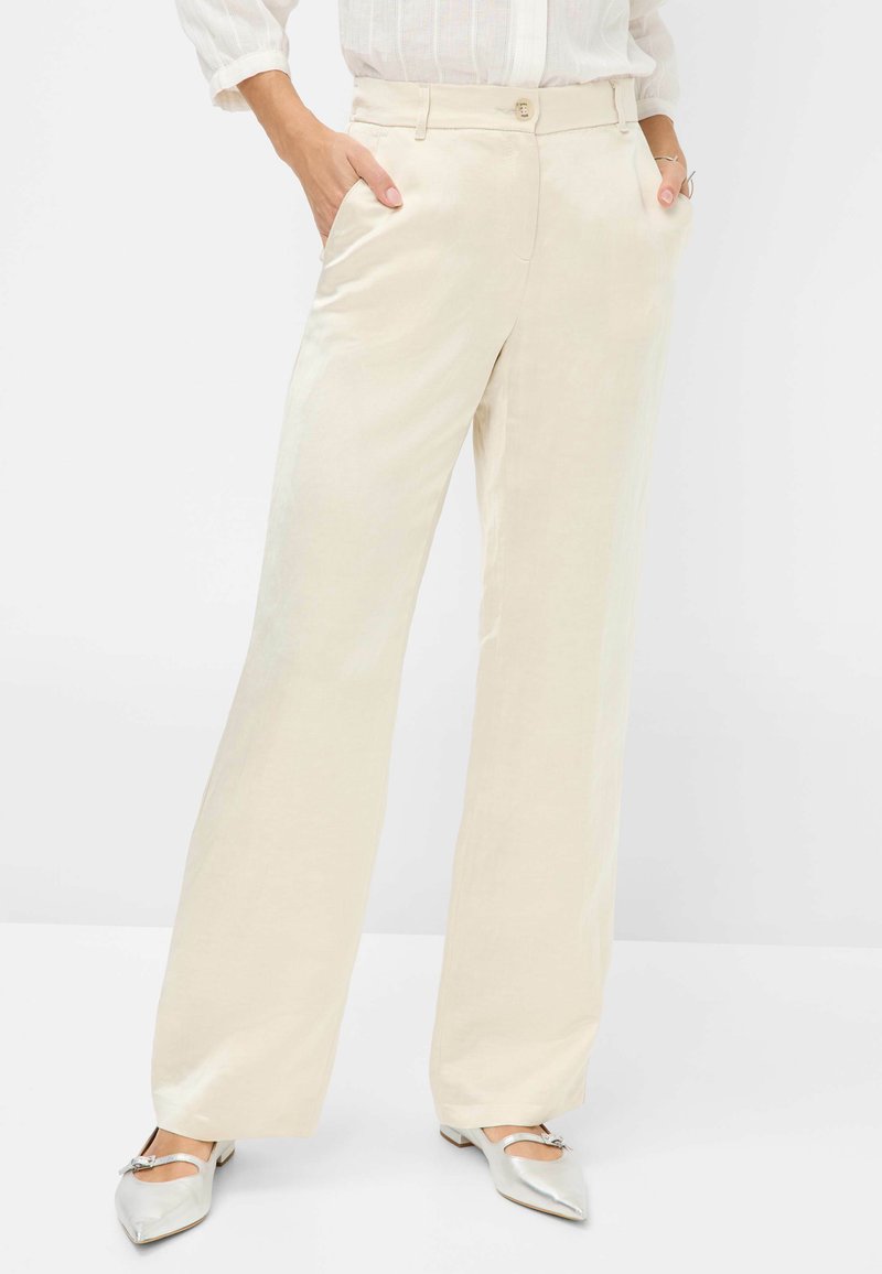 Beige wijde broek van lichtgewicht stof met zijzakken en een knoopsluiting. Gecombineerd met zilverkleurige schoenen met puntige neuzen.