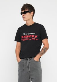 Black cotton t-shirt with red and white text reading “Highperformance 1981 REPLAY.” Grey jogger pants with a drawstring waist. Black sunglasses.