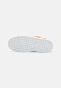 Semelle en caoutchouc blanche d'une chaussure de sport orange présentant un motif de bande de roulement texturé croisé et un petit logo rectangulaire au centre.