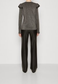 Top lungo grigio scintillante con dettagli arricciati sulle spalle, abbinato a pantaloni in pelle nera aderenti, visto da dietro.