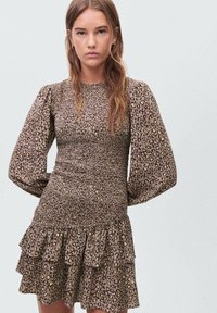 Haljina sa leopard uzorkom u smeđoj i bež boji, sa napuštenim rukavima, uskim korzetom i višeslojnim volanom na donjem rubu. Tekstuirana tkanina.