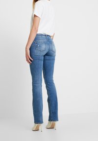 Jeans de mezclilla azul con un diseño ajustado, ligero desgaste en los bolsillos traseros y un estilo acampanado, combinados con unos zapatos de tacón alto beige.