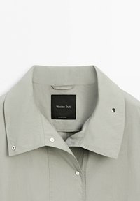 Light gray collared jacket with snap buttons and visible black Massimo Dutti label centered inside the neckline.