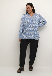 Blusa a maniche lunghe blu e bianca con motivo, scollo a V e dettagli con bottoni, abbinata a pantaloni neri e sandali neri chunky.