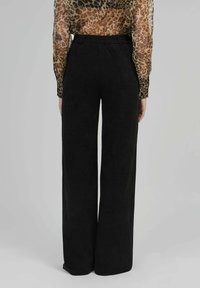 Pantalons larges noirs en tissu doux, dotés d'une taille élastique haute. Des coutures visibles à l'ourlet ajoutent du détail.