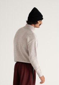 Helles graues Strickpullover mit einem Trichterkragen, der melierte, mehrfarbige Fasern aufweist. Kombiniert mit dunkelbeerigen Hosen, die einen lockeren Schnitt präsentieren.