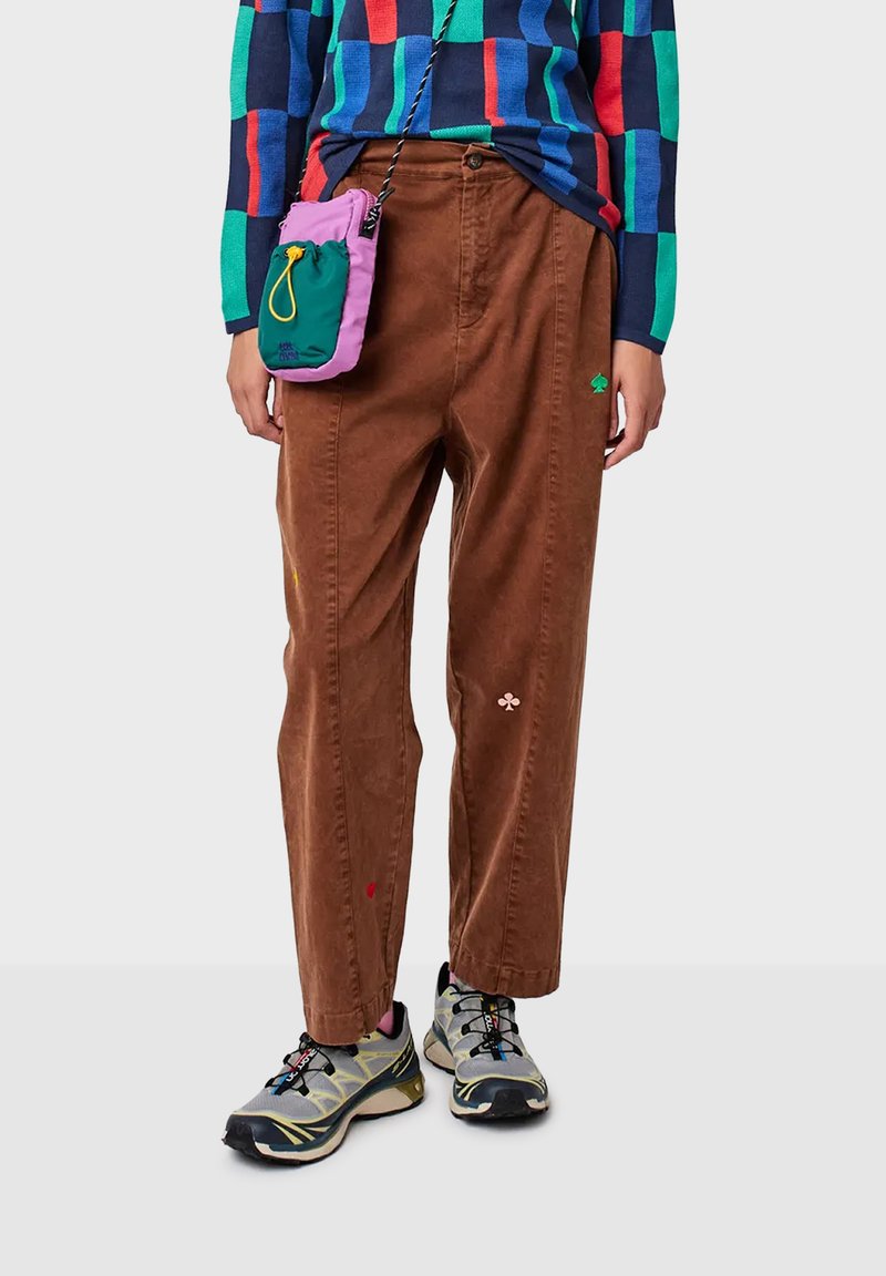 Pantalones de pana marrones con un corte holgado, que presentan acentos bordados coloridos y bolsillos laterales. Combinados con zapatillas grises y negras.