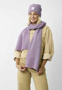 Lila gestrickte Mütze und Schaal-Set, mit einem gerippten Muster und einem quadratischen Logopatch auf der Mütze. Tragen dazu eine beigefarbene Utility-Jacke.