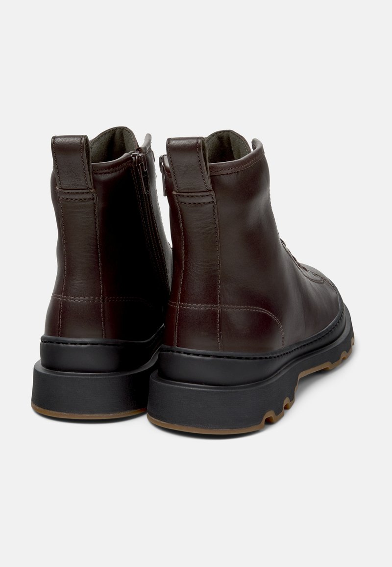 Donsbruine leren enkelboots met een textuur oppervlak, binnenrits en een contrasterende zwarte rubberen zool. Ronde vorm met een lichte hak.
