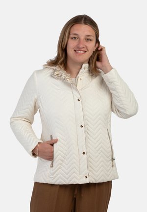 Giacca bianca trapuntata con motivo a zigzag, dotata di colletto alto, bottoni a scatto e tasche con zip. Accentuata da cuciture decorative.