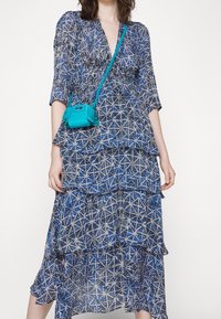 Vestido azul con estampado de tres capas, con un pronunciado escote en V y mangas de 3/4. Combinado con un pequeño bolso cruzado de color turquesa.