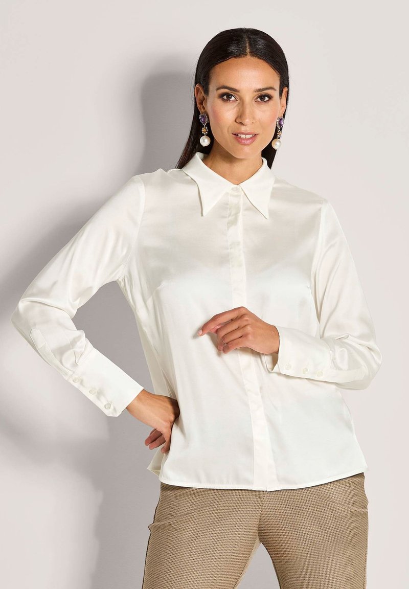 Witte satijnen blouse met lange mouwen, een gestructureerde kraag, knoopsluiting aan de voorkant en manchetten, gecombineerd met gestructureerde bruine broek.