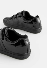 Svarta lacklädersneakers med en slät ytfinish, kardborreband, rund tå och texturerad svart gummisula.