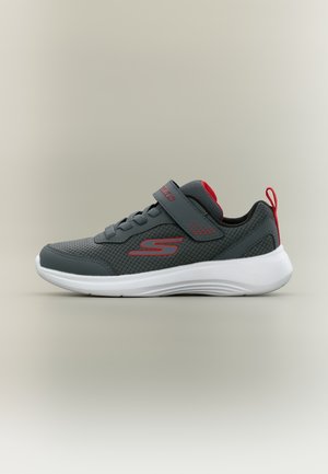 Sneaker grigio scuro con accenti rossi, suola bianca, tomaia in mesh, lacci e una fascia in velcro, mostrata di lato su uno sfondo neutro.