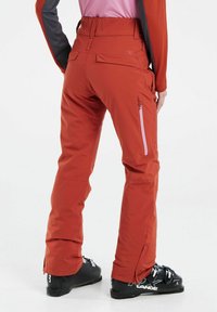 Pantaloni da sci rossi con design aderente, dotati di due tasche laterali con zip e zip alla caviglia. Realizzati in un materiale resistente e impermeabile.