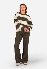 Φυσική πλεκτή ζακέτα με οριζόντιες γκρι και κρεμ ρίγες, σε συνδυασμό με χαλαρές σκούρες γκρι παντελόνες. Η ζακέτα έχει φαρδιά λαιμόκοψη και ριμπ μανσέτες.