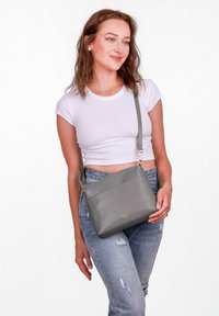 Šedá kožená křížová taška se zipov�ým uzávěrem, vyznačující se hladkým povrchem a jednoduchým designem. Velká přední kapsa a nastavitelné ramenní popruhy.