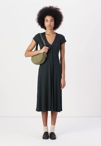Dunkelgrünes, knielanges Kleid mit V-Ausschnitt, kurzen Ärmeln und Knöpfen vorne. Kombiniert mit einer runden olivfarbenen Tasche und schwarzen Schuhen.
