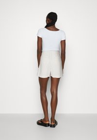 Camiseta blanca ajustada combinada con shorts de rayas finas en beige claro, con abertura en el dobladillo y dos bolsillos traseros. Sandalias negras tipo slide completan el conjunto.