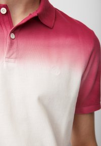 Polo en dégradé de couleur, allant du rose foncé au blanc. Il présente un col, deux boutons et un logo discret sur la poitrine.