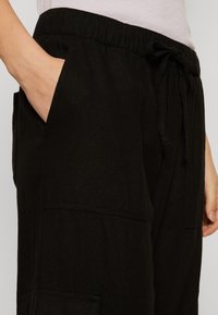 Černé cargo kalhoty s elastickým pasem, stahovací šňůrkou, boční kapsou a volným střihem, vyrobené ze měkkého, strukturovaného materiálu.