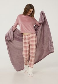 Top in velluto rosa con maniche ampie, pantaloni del pigiama a quadri in rosa, bianco e viola, e pantofole soffici bianche con accenti di animali.