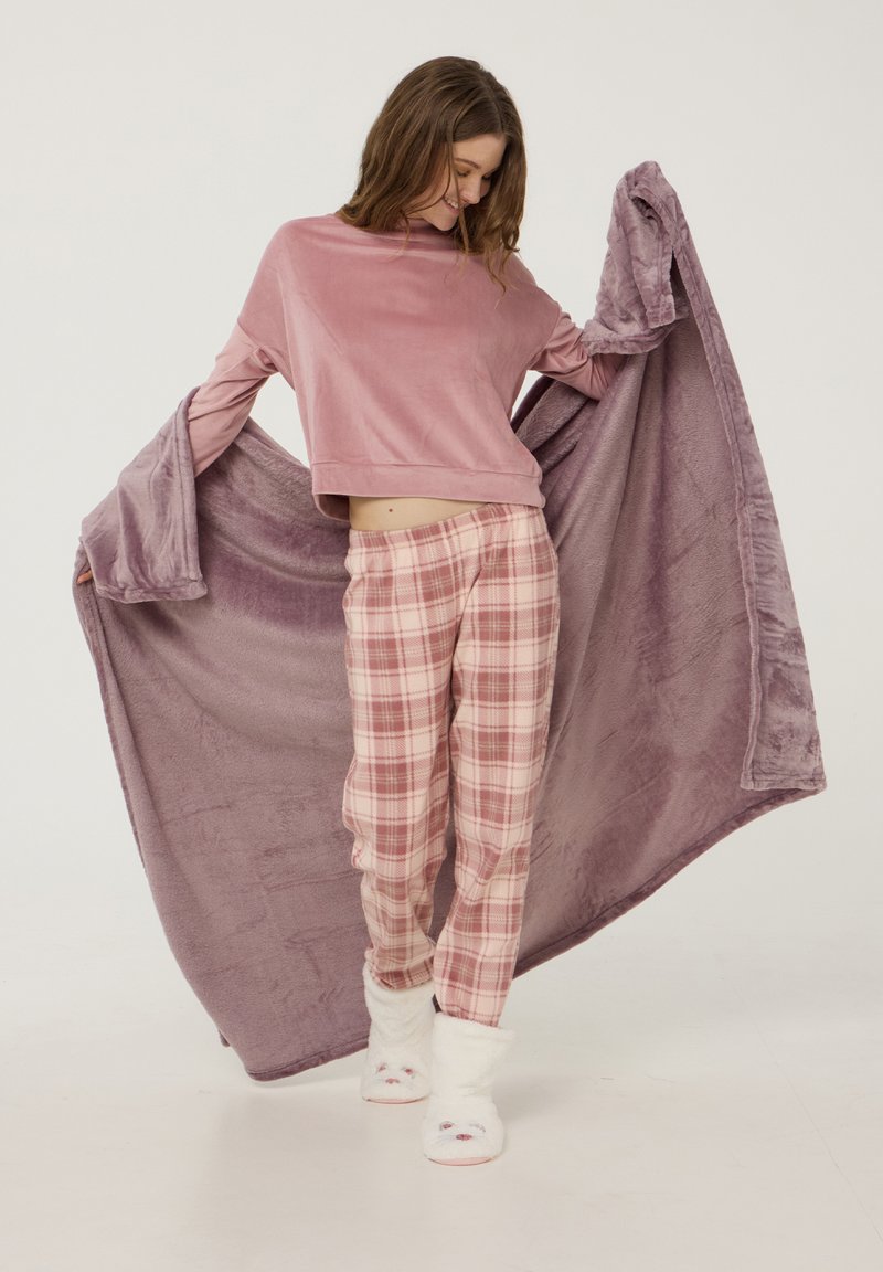 Top in velluto rosa con maniche ampie, pantaloni del pigiama a quadri in rosa, bianco e viola, e pantofole soffici bianche con accenti di animali.