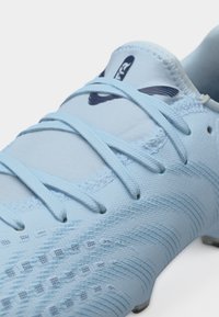 Scarpa da calcio azzurro chiaro con tomaia testurizzata, lacci incrociati e logo nero sulla lingua, su sfondo bianco.