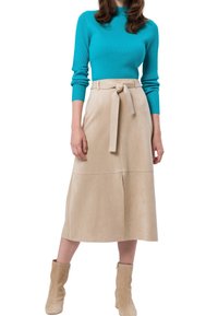 Beige faux suede midi skirt dengan ikat pinggang, memiliki potongan lurus dan belahan samping. Dipadukan dengan atasan lengan panjang bertekstur rib yang berwarna turquoise.