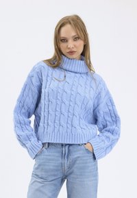Light blue cable-knit sweater with a high collar and ribbed hem. Features oversized sleeves and a cropped design, paired with light denim jeans.