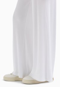 Pantaloni larghi a coste bianchi, in tessuto morbido, abbinati a scarpe da ginnastica bianche con suola beige e dettagli perforati.