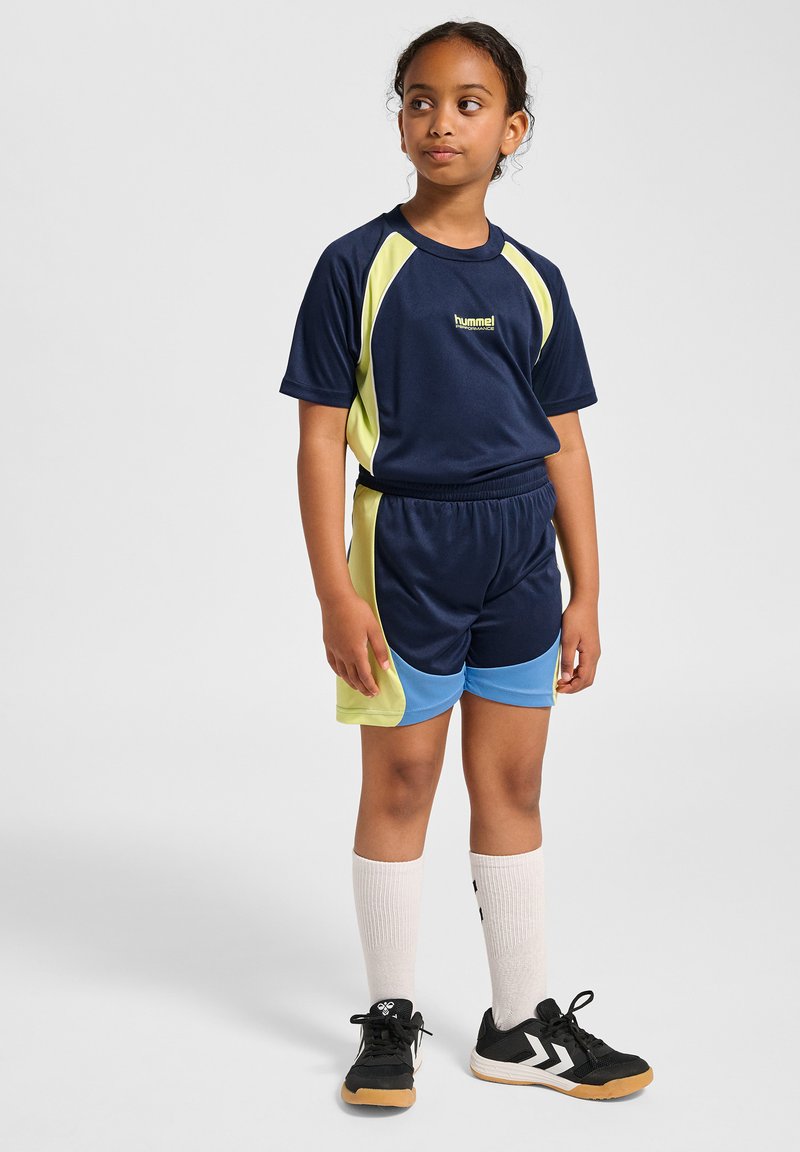 Marinblå idrottströja med limegröna detaljer, kombinerad med marinblå och blå shorts. Svarta sneakers och vita knälånga strumpor fulländar utseendet.