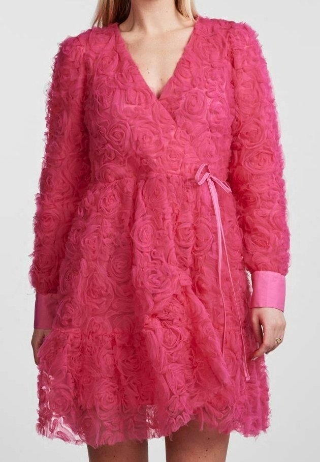 Femme portant une robe rose vif avec des motifs de roses texturés, des manches longues, un style cache-cœur et un ruban noué à la taille.