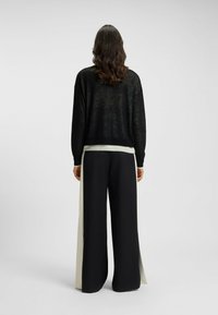 Black knitted sweater with a wide fit and long sleeves; paired with high-waisted black trousers featuring cream side panels.