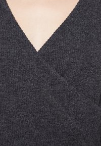 Szary teksturowany materiał o dekolcie w kształcie V, z delikatnym prążkowanym wzorem i falbaniastymi brzegami. Minimalistyczna i zwięzła konstrukcja.