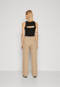 Top negru fără mâneci cu o decupare pe spate, asortat cu pantaloni evazați bej. Textura fină a materialului, design minimalist și croială adaptată.