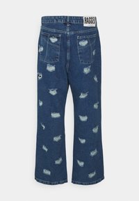Jeans de denim azul desgastado con un corte relajado, que presentan grandes desgastes, detalles deshilachados y una cinturilla con logo en la parte posterior.