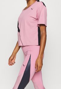 Rosa idrottstop med svarta detaljer, korta ärmar och rundad halsringning. Ett par åtsittande rosa leggings med svarta sidopaneler och nättextur.