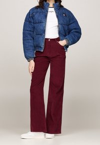 Niebieska kurtka pikowana z pikowanym wzorem i elastycznymi mankietami, w połączeniu z bordo sztruksowymi spodniami z rozszerzanymi nogawkami oraz białymi trampkami.