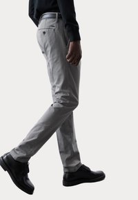 Pantaloni di cotone grigi con una vestibilità slim, dotati di una tasca posteriore e una leggera lucentezza, abbinati a scarpe di pelle nere.