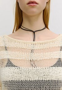 Schwarzer Choker mit verstellbaren Bändern um ein leicht gestricktes, cremefarbenes und schwarzes gestreiftes Oberteil mit einem offenen Ausschnitt.