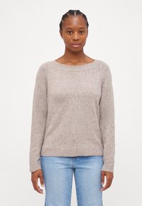 Maglione marrone chiaro, morbido, con scollatura rotonda, maniche lunghe, polsini e orlo a costine, indossato sopra dei jeans in denim azzurro chiaro.