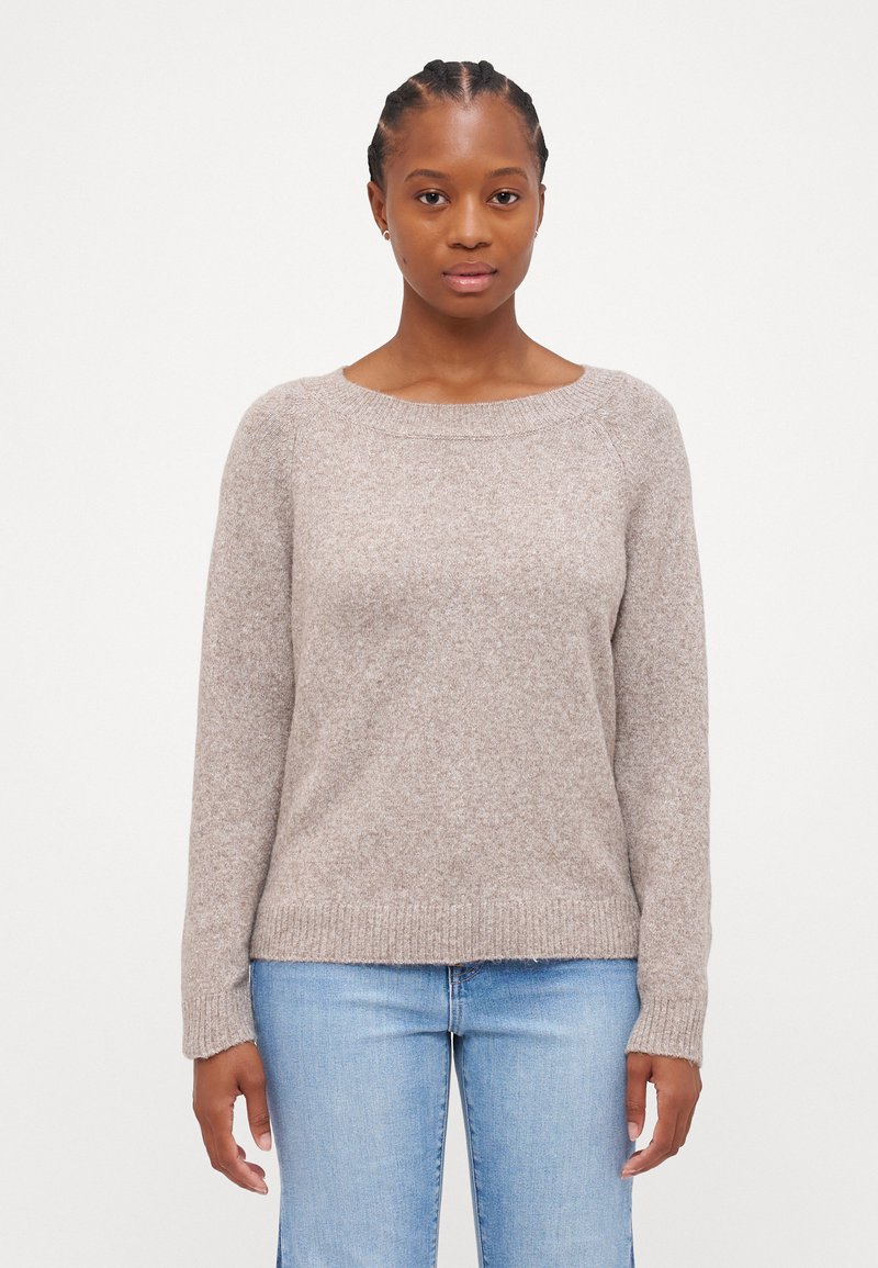Maglione marrone chiaro, morbido, con scollatura rotonda, maniche lunghe, polsini e orlo a costine, indossato sopra dei jeans in denim azzurro chiaro.