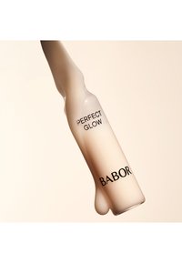 Sérum Perfect Glow de Babor dans un flacon en verre allongé et givré avec du texte noir ; une texture crémeuse s'écoule du nez.