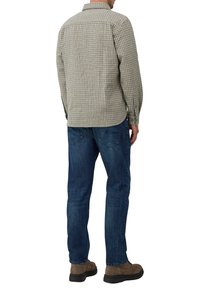 Man in een beige geruite lange mouwen overhemd, blauwe jeans en een paar bruine suède schoenen, van achteren kijkend op een witte achtergrond.