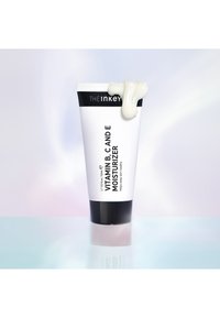 Vit tube med svarta accenter, märkt "Vitamin B, C och E fuktighetskräm." Slät, krämig produkt som sippra ur toppen. Minimalistisk design.