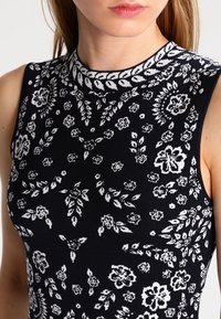 Svart stickad topp med vitt blommönster, med rund halsringning och ärmlös design. Mjuk textur med figursydd design.